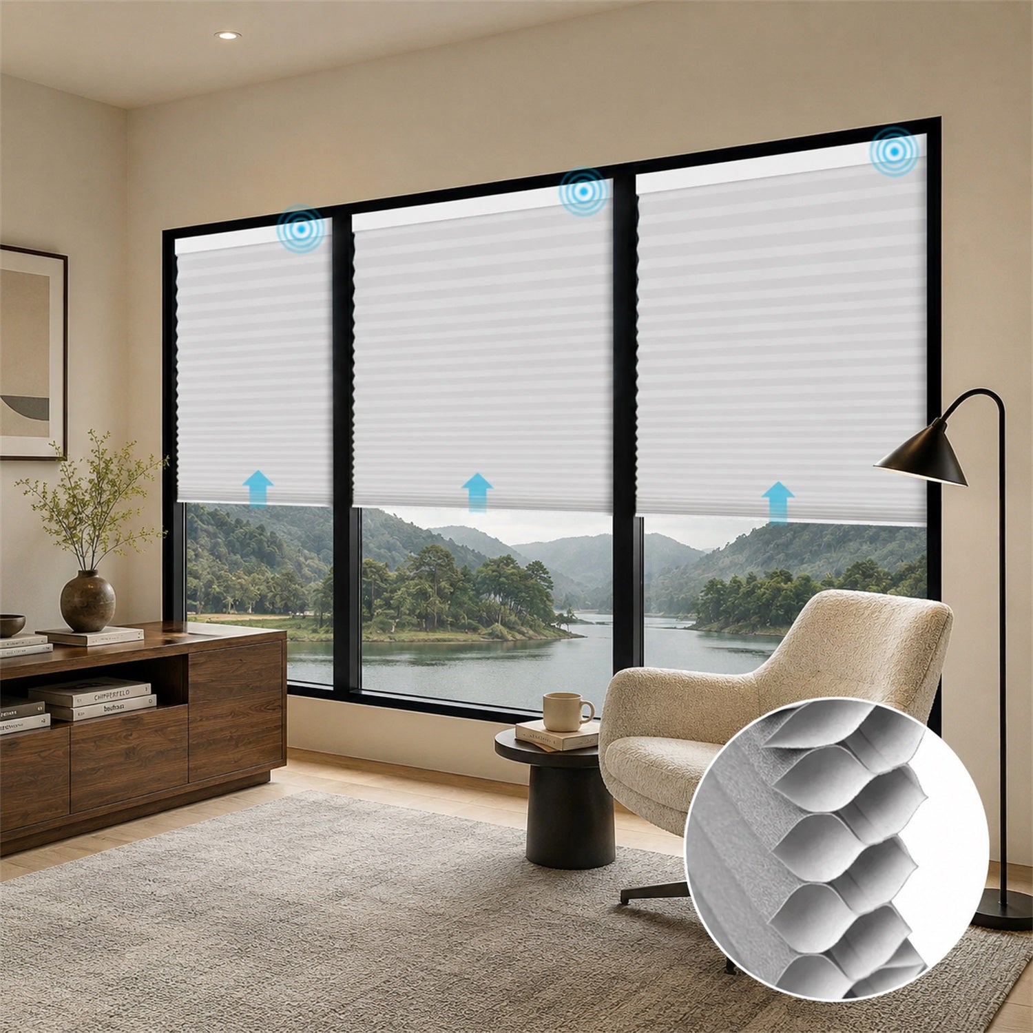 A set of white cellular roller blinds installed on a large black-framed window in a modern living room. The image includes blue arrow overlays indicating airflow and a circular inset showing a close-up of the textured honeycomb pattern of the blinds.