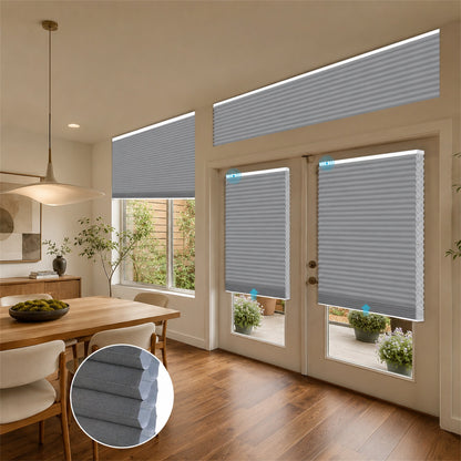 Gray cellular window and door blinds installed in a modern dining room and patio area, with an inset circular detail of the fabric texture.