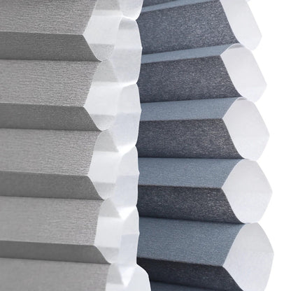 Close-up of gray pleated window blinds with a hexagonal design, showing both the light gray outer fabric and the darker charcoal inner lining.