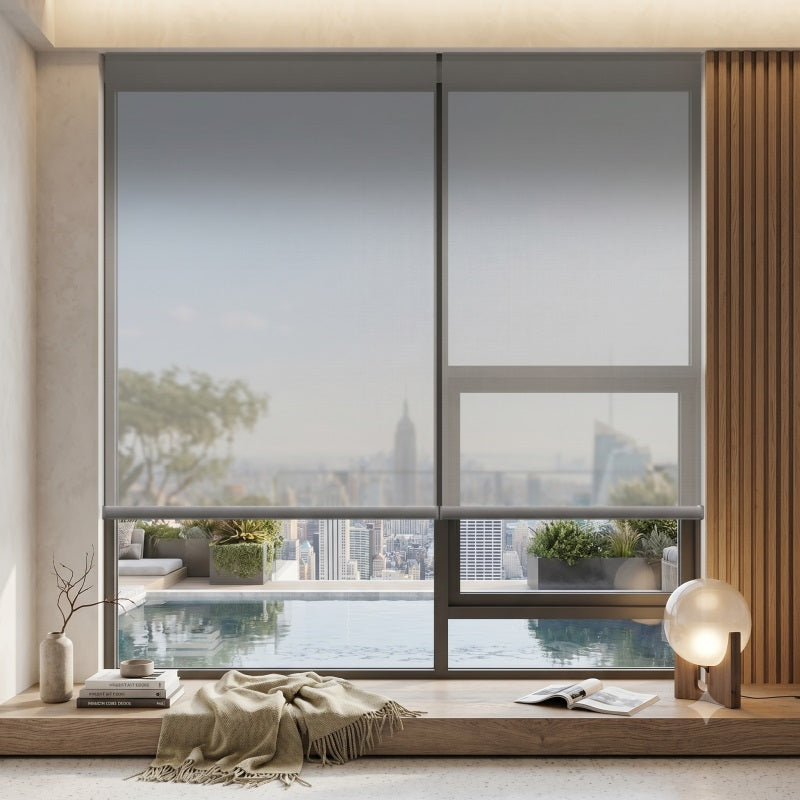 A modern interior scene showing a large window with roller shades partially drawn, overlooking a city skyline and infinity pool. A wooden ledge with a throw blanket, books, plants, and a lamp is visible in the foreground.